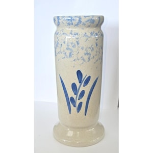 Puede incluir: Un jarrón alto de cerámica beige con una base ancha y un borde acampanado. El jarrón presenta detalles moteados azules alrededor del borde y un diseño floral azul. El jarrón mide aproximadamente 30 cm de alto.