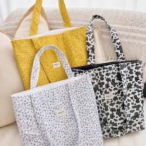 May include: Four tote bags in various patterns. One is yellow with white starbursts, another is white with blue floral print, and the third is black and white cow print. Each bag has a matching handle and a small label that reads "GAVRE & EVE".