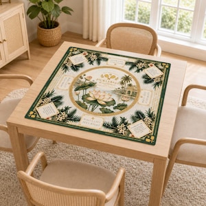 May include: A square, green-bordered game mat with a central floral design and the text "Pickleball Mahjong". The mat is set on a light wood table, surrounded by four chairs. The design includes a lotus flower and tropical imagery.