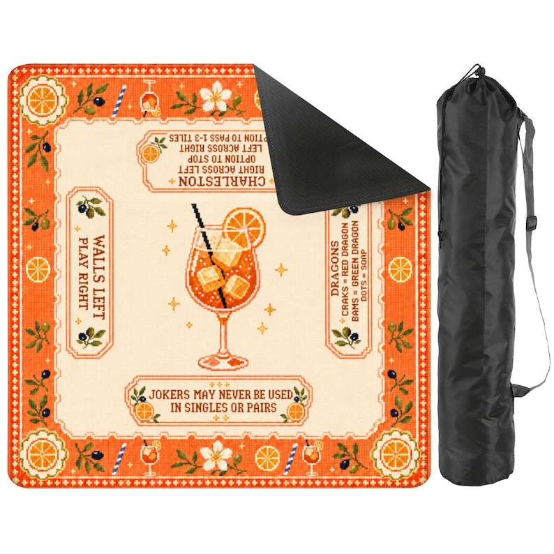 Op de afbeelding: Een vierkante speelmat met een oranje rand met citrus- en bloemmotieven, een centrale cocktailillustratie en tekst inclusief Charleston, Walls Left Play Right en Dragons-regels. Een zwarte draagtas met schouderriem is inbegrepen.