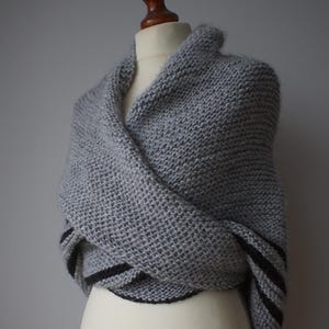 May include: A gray knitted shawl with black stripes on the edges, draped over a white mannequin.