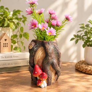 May include: A cylindrical vase designed to resemble a textured tree trunk with brown bark and a light-colored interior. Three small red mushrooms with white spots are attached to the front. The vase holds a bouquet of bright pink flowers.