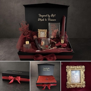 May include: A black gift box tied with a red ribbon, filled with a candle, a glass, a small framed picture, and other decorative items. The box is inscribed with "Inspired by Art Made to Treasure" in gold.