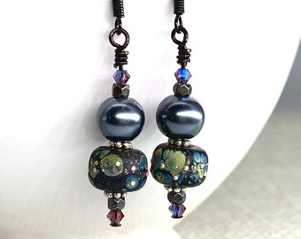 May include: A pair of dangle earrings with black beads and a blue and green patterned bead. The earrings have a silver wire and a black hook.