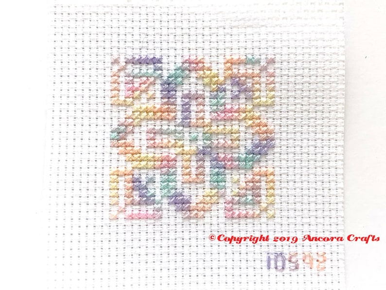 ThreadworX 10592 Variegated Rainbow Embroidery Floss Wildflowers thread has a gradient of pastel pink, orange, yellow, green, blue, and purple and is shown here stitched in a geometric cross stitch pattern.