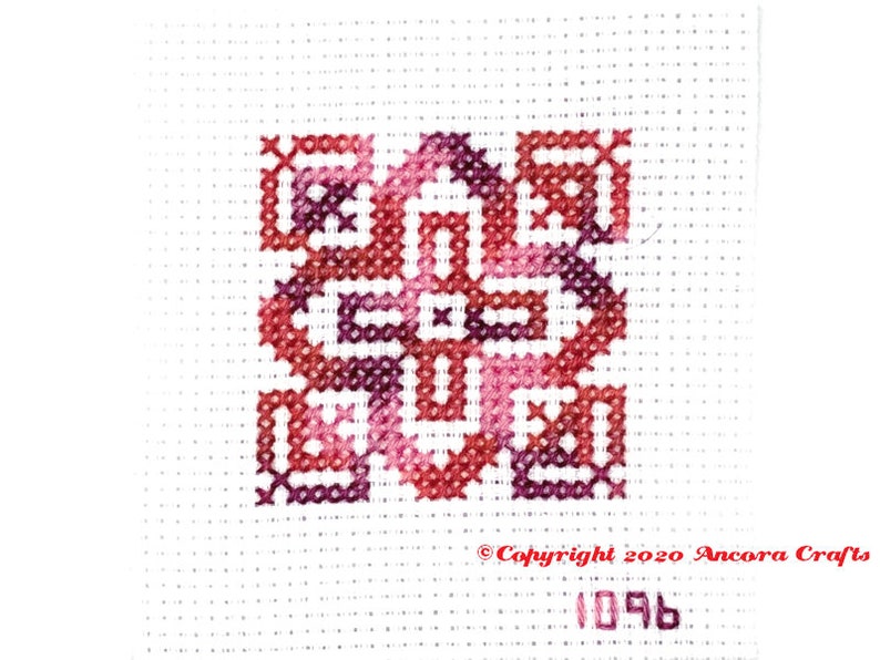 ThreadworX 1096 Variegated Embroidery Floss Renaissance thread has a repeating gradient of dark corals, pink, and red-purple and is shown here stitched in a geometric cross stitch pattern.