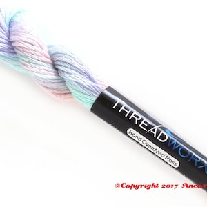 May include: A skein of hand-dyed embroidery floss in shades of light blue, pink, and green. The floss is wrapped around a black label that reads "THREADWORK Hand Overdyed Floss Copyright 2017 Ancora Crafts".