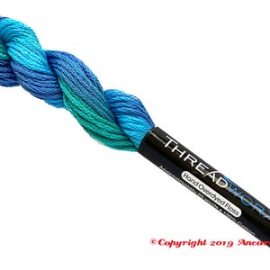 May include: A skein of hand-dyed embroidery floss in shades of blue and green. The floss is wrapped around a black label that reads "THREADWORX Hand Overdyed Floss Approximately 20 yards - 100% Cotton Copyright 2019 Ancora Crafts".