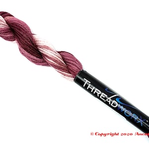 May include: A skein of embroidery floss in a deep burgundy colour with white and light pink accents. The floss is wound around a black spool with the text "THREADWORK" printed in white.