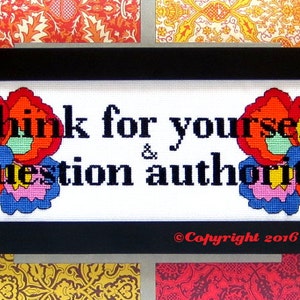 Pode incluir: Bordado de ponto cruz emoldurado com fundo branco e texto preto que diz "Think for yourself & question authority". O texto é rodeado por dois desenhos florais coloridos.