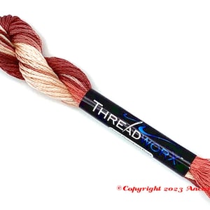 May include: A skein of embroidery floss in a red, white, and cream color combination. The floss is wrapped around a black card with the text "THREADWORK" in blue and white lettering.