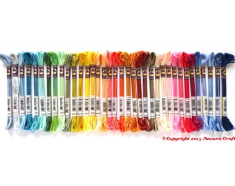 May include: A rainbow assortment of 42 embroidery floss skeins, each with a white label and black text indicating the color number. The skeins are arranged in a row from left to right, starting with light blue and ending with dark blue.