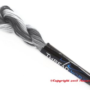Puede incluir: Un ovillo de hilo de bordar blanco y negro con una etiqueta negra que dice "THREADWORK" y "Copyright 2018 Ancona Crafts".