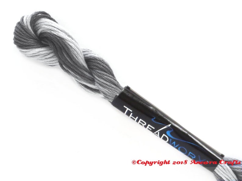 Puede incluir: Un ovillo de hilo de bordar blanco y negro con una etiqueta negra que dice "THREADWORK" y "Copyright 2018 Ancona Crafts".
