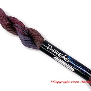 May include: A skein of hand-dyed embroidery floss in shades of purple, brown, and gray. The floss is wrapped around a black label that reads "THREADWORX Hand Overdyed Floss" and "Copyright 2020 Ancona Crafts".