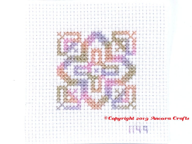 ThreadworX 1149 Variegated Rainbow Embroidery Floss Rainbow Fairy thread has a repeating gradient of soft pink, orange, green, and blue-purple, and is shown here stitched in a geometric cross stitch pattern.