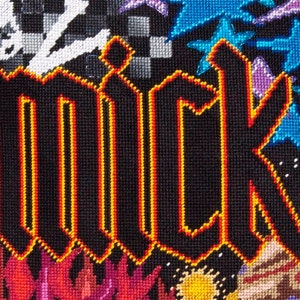 May include: A black and yellow cross-stitch embroidery with the word "MICK" in a bold, gothic font. The background features a variety of colorful designs, including stars, flowers, and planets.