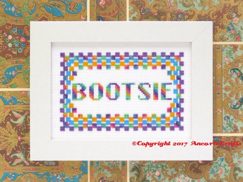 This ThreadworX 1154 rainbow embroidery floss is a gorgeous variegated blend of bright pink, orange, yellow, green, blue, and purple, and is shown here stitched in a project with lettering that reads Bootsie and in a geometric pattern border.