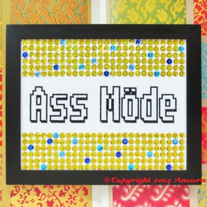 Może przedstawiać: Ramka z haftem krzyżykowym z tekstem "ASS MODE" w kolorze czarno-białym. Ramka jest czarna i ma obramowanie z żółtych i niebieskich kryształków.