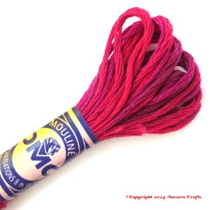 May include: A skein of DMC embroidery floss in a pink and magenta color gradient. The floss is wrapped around a blue and yellow label with the DMC logo and the text "Mouline" printed on it.