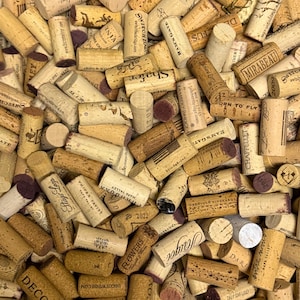 May include: A close-up shot of a pile of used wine corks. The corks are various shades of brown and beige, with some showing printed text and logos. The ends of the corks are a reddish-purple color. The image conveys a rustic, vintage theme.