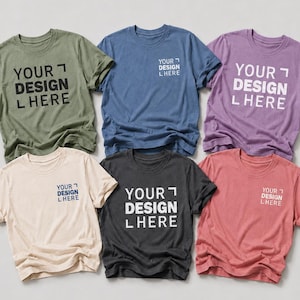 Puede incluir: Una colección de seis camisetas de manga corta y cuello redondo en colores verde oliva, azul, morado, crema, gris carbón y rosa empolvado. Cada camiseta presenta el texto impreso YOUR DESIGN HERE en blanco o azul oscuro en el pecho.