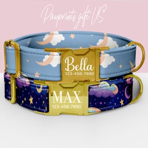 May include: Two personalized dog collars. The top collar is light blue with a pattern of moons, clouds, and stars. The bottom collar is dark blue with a similar celestial design. Both have gold-colored buckles with names and phone numbers.