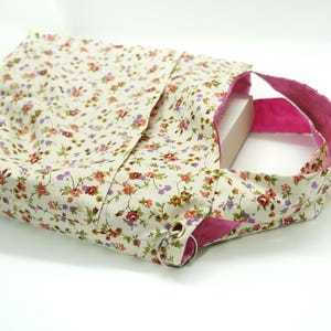 May include: A floral print tote bag with a cream background and small red, purple, and green flowers. The interior and straps are a bright pink. The bag has a rectangular shape and a metal ring detail.