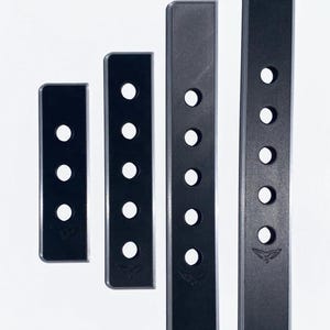 May include: Four rectangular black strips of varying lengths arranged vertically. Each strip features a series of circular holes and a small embossed bird-like logo at the bottom. The strips have a smooth matte finish with thin grey edges.