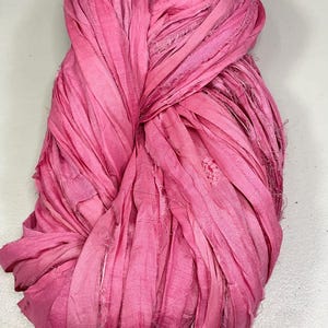 May include: A bundle of vibrant pink silk ribbon, tightly knotted. The ribbon has a textured, frayed appearance, with varying shades of pink throughout. Ideal for crafting, scrapbooking, or adding a touch of color to any project.