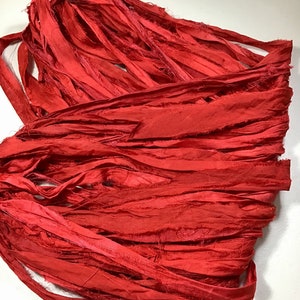 K&ouml;nnte beinhalten: Ein B&uuml;ndel leuchtend roter Seidenb&auml;nder, eng gewickelt. Das Band hat einen leicht ausgefransten Rand, der Textur verleiht. Die Farbe ist ein sattes, ges&auml;ttigtes Rot, ideal f&uuml;r Bastelarbeiten oder Dekorationszwecke.