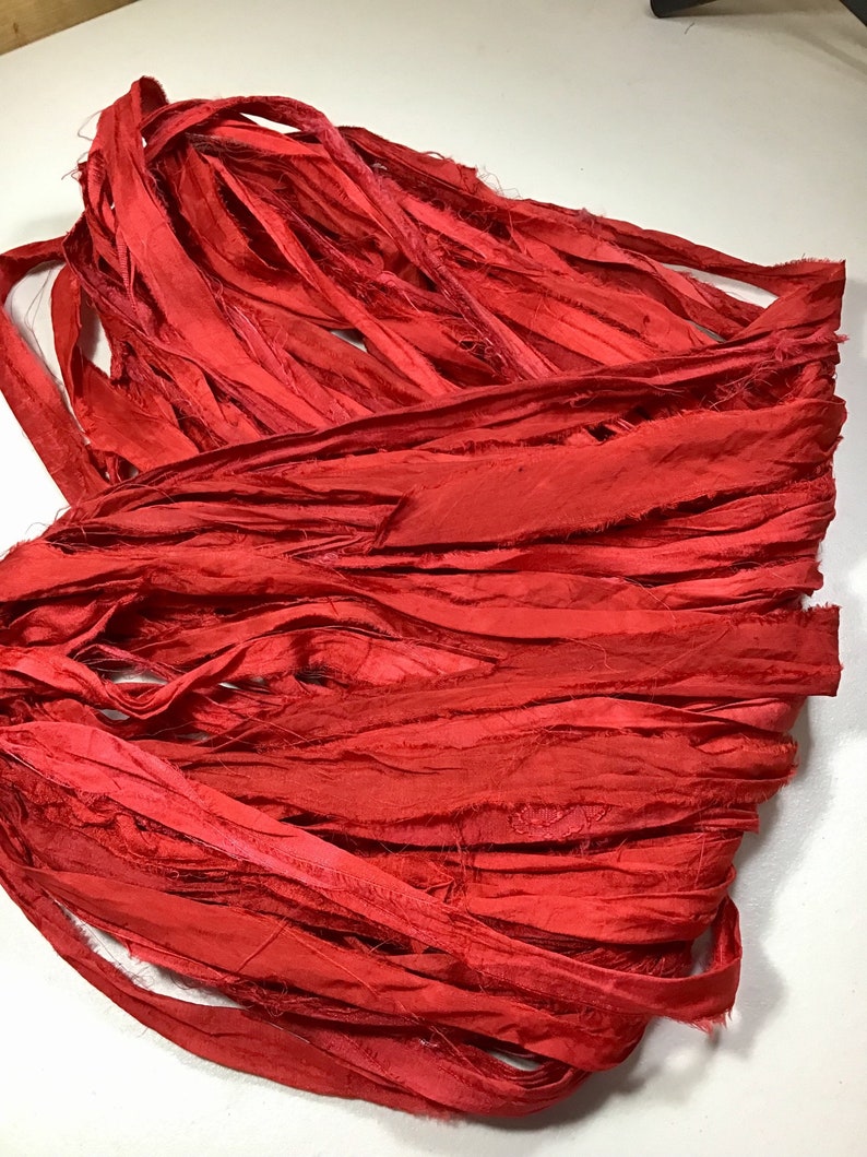 K&ouml;nnte beinhalten: Ein B&uuml;ndel leuchtend roter Seidenb&auml;nder, eng gewickelt. Das Band hat einen leicht ausgefransten Rand, der Textur verleiht. Die Farbe ist ein sattes, ges&auml;ttigtes Rot, ideal f&uuml;r Bastelarbeiten oder Dekorationszwecke.