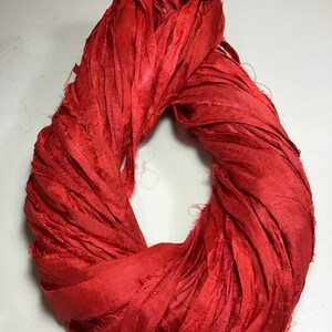 K&ouml;nnte beinhalten: Ein leuchtend rotes Seidenband, eng gewickelt. Das Band hat eine strukturierte, leicht ausgefranste Optik, die auf eine handgefertigte oder handwerkliche Qualit&auml;t hindeutet. Die Farbe ist ein sattes, ges&auml;ttigtes Rot, geeignet f&uuml;r Bastel- oder Dekorationszwecke.