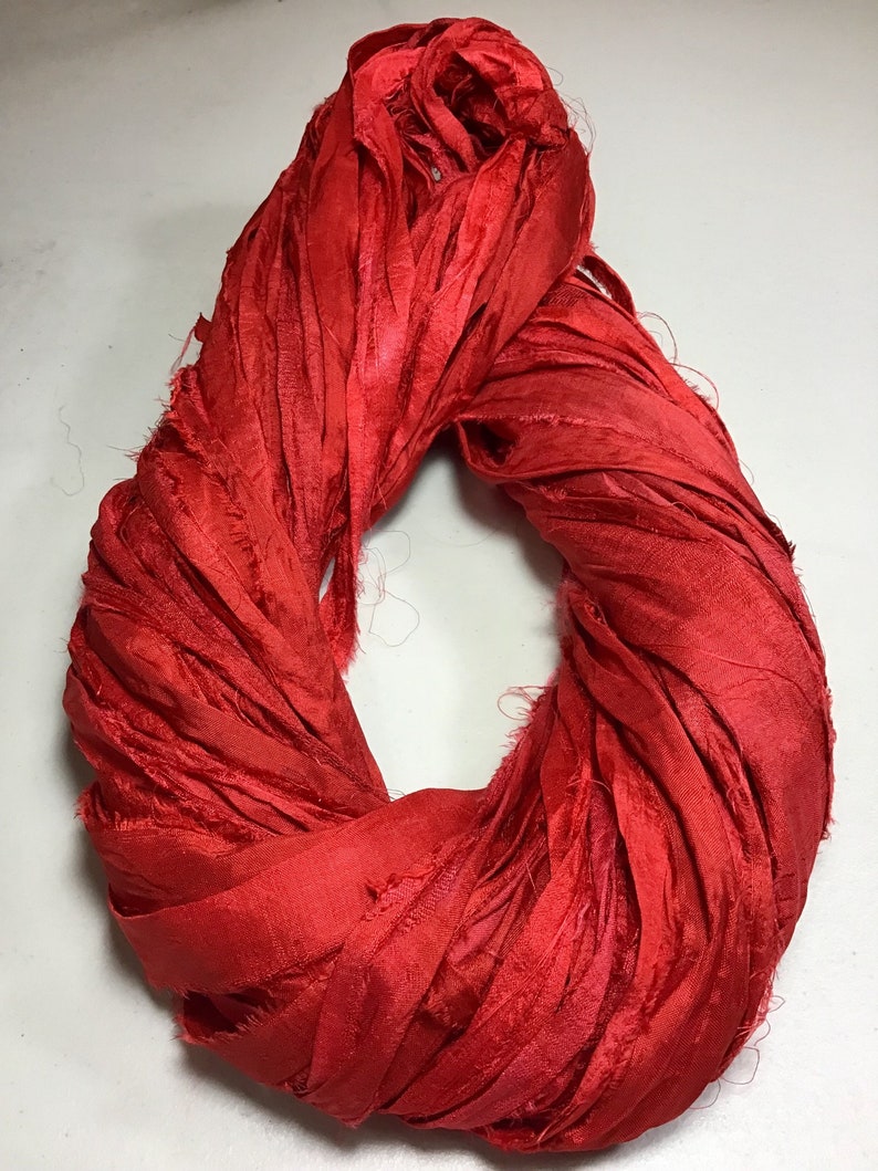 K&ouml;nnte beinhalten: Ein leuchtend rotes Seidenband, eng gewickelt. Das Band hat eine strukturierte, leicht ausgefranste Optik, die auf eine handgefertigte oder handwerkliche Qualit&auml;t hindeutet. Die Farbe ist ein sattes, ges&auml;ttigtes Rot, geeignet f&uuml;r Bastel- oder Dekorationszwecke.