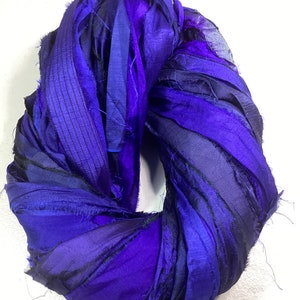 May include: A circular arrangement of layered, textured fabric in shades of blue and purple. The fabric appears to be silk or a similar material, with a slightly frayed edge. The color gradient ranges from deep indigo to vibrant violet.
