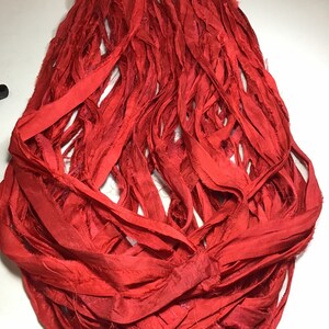 K&ouml;nnte beinhalten: Ein B&uuml;ndel leuchtend roter Seidenb&auml;nder, locker und flie&szlig;end angeordnet. Das Band scheint handgeschnitten zu sein, mit ausgefransten Kanten, die Textur verleihen. Die Farbe ist ein sattes, ges&auml;ttigtes Rot, geeignet f&uuml;r Bastelarbeiten oder Dekorationszwecke.