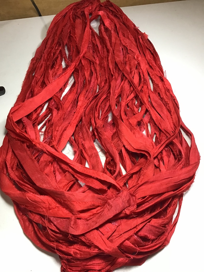 K&ouml;nnte beinhalten: Ein B&uuml;ndel leuchtend roter Seidenb&auml;nder, locker und flie&szlig;end angeordnet. Das Band scheint handgeschnitten zu sein, mit ausgefransten Kanten, die Textur verleihen. Die Farbe ist ein sattes, ges&auml;ttigtes Rot, geeignet f&uuml;r Bastelarbeiten oder Dekorationszwecke.