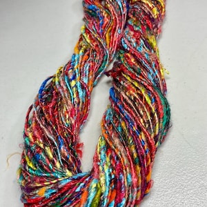 May include: A vibrant skein of yarn with a mix of colors including red, blue, yellow, and orange. The yarn appears to be made of multiple strands, creating a textured look. Ideal for knitting, crocheting, or other fiber art projects.