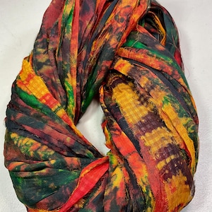 May include: A colorful infinity scarf made of strips of fabric in shades of red, orange, yellow, green, and black. The scarf is twisted into a circular shape, showcasing the vibrant, textured material.