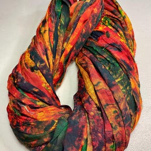 May include: A colorful infinity scarf with a vibrant mix of red, orange, yellow, and green hues. The scarf appears to be made of a soft, flowing fabric, possibly silk or a similar material. The design features a tie-dye or watercolor effect, creating a unique and artistic accessory.