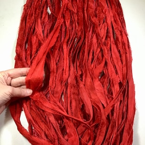 May include: Close-up of a bundle of vibrant red silk ribbon. The ribbon is made of long, thin strips with a slightly frayed texture. The color is a rich, solid red, and the ribbon appears to be soft and flowing. The image is well-lit, highlighting the texture and color.
