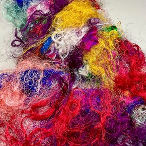 May include: A vibrant pile of colorful silk fibers in shades of red, yellow, blue, purple, and green. The fibers are loosely spun and have a textured, slightly crimped appearance. Ideal for textile art, weaving, or other craft projects.