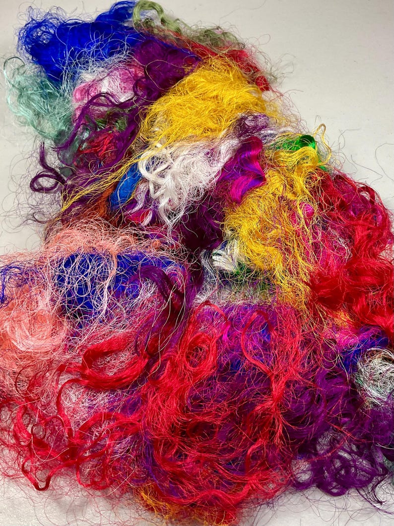 May include: A vibrant pile of colorful silk fibers in shades of red, yellow, blue, purple, and green. The fibers are loosely spun and have a textured, slightly crimped appearance. Ideal for textile art, weaving, or other craft projects.