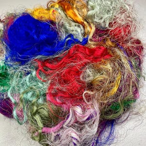 May include: A vibrant assortment of colorful fibers, including shades of blue, red, green, yellow, and purple. The fibers are tightly curled and appear to be made of silk or a similar material. The image showcases a variety of textures and hues.