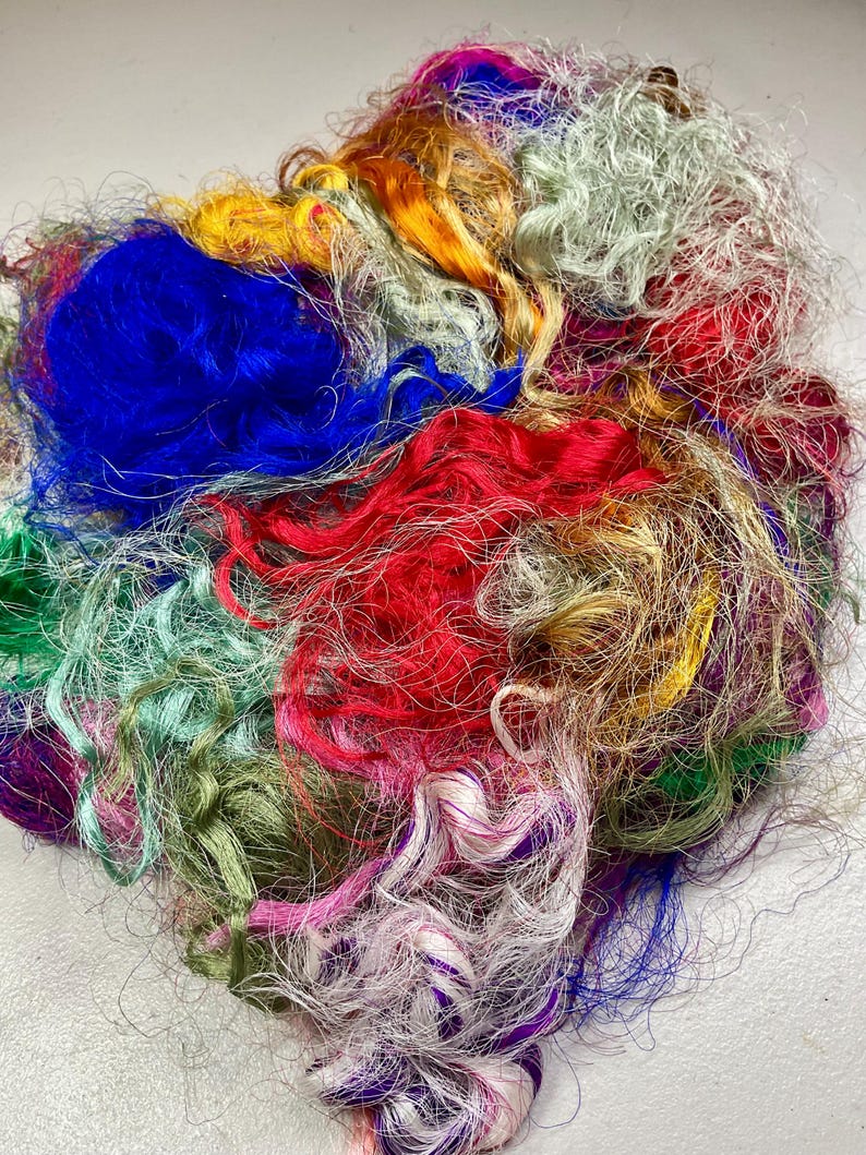 May include: A vibrant assortment of colorful fibers, including shades of blue, red, green, yellow, and purple. The fibers are tightly curled and appear to be made of silk or a similar material. The image showcases a variety of textures and hues.