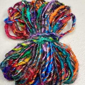 May include: A vibrant bundle of colorful yarn, featuring a mix of red, orange, blue, green, and purple hues. The yarn is tightly wound and tied together, showcasing a variety of textures and shades. This craft supply is ideal for knitting, crocheting, or other fiber art projects.
