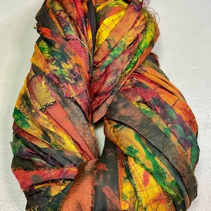 May include: A colorful, handmade fabric wreath. The wreath is made of strips of fabric in shades of red, orange, yellow, green, and black. The fabric has a textured appearance and is arranged in a circular shape. The wreath is likely for home decor.