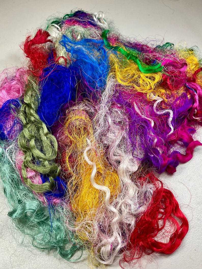 May include: A vibrant assortment of colorful craft fibers. The image showcases a mix of textures and hues, including red, blue, green, yellow, pink, and purple. The fibers appear to be silk or a similar material, ideal for various crafting projects.