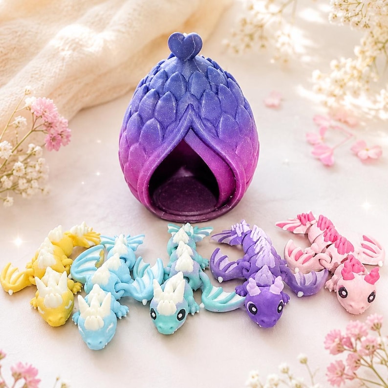 May include: A purple and blue gradient dragon egg with a heart-shaped topper, accompanied by five small articulated dragon figurines in yellow, light blue, teal, purple, and pink, each featuring white accents and detailed scale textures.