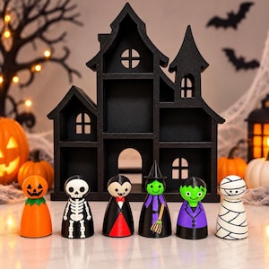May include: A black wooden haunted house display shelf featuring six small peg dolls representing Halloween characters: a pumpkin, a skeleton, a vampire, a witch with a broom, a green monster, and a mummy, all arranged in a row.